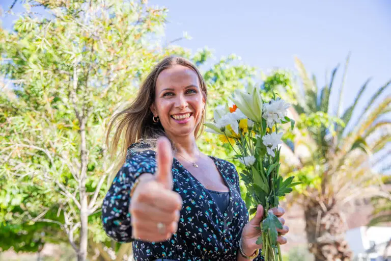 A smiling woman is holding a bouquet of flowers and giving a thumbs up